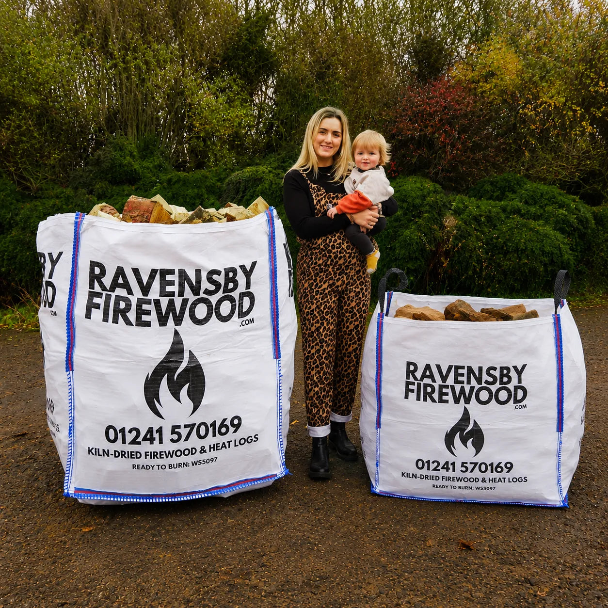 Woman holding a child next to two large bulk bags of kiln dried firewood in Arbroath.