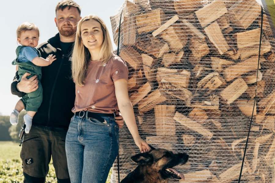 Emma from Ravensby Firewood and family standing next to a kiln-dried log pile in Angus