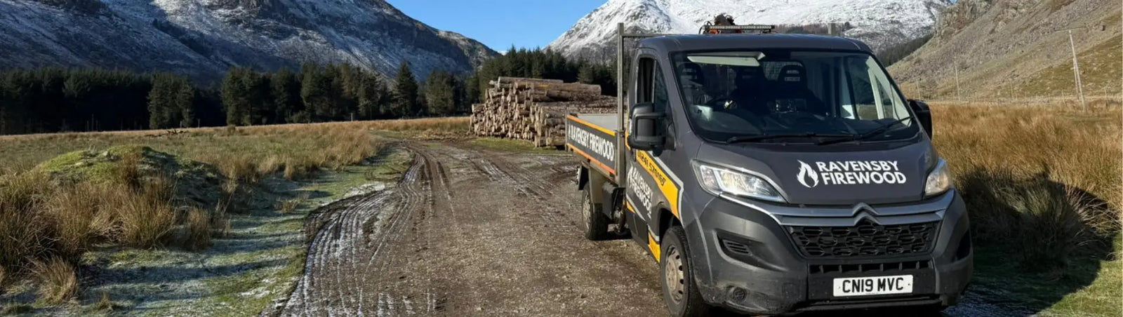 Van with Ravensby Firewood branding next to a pile of cut, stacked firewood logs in rolling Perthshire hills