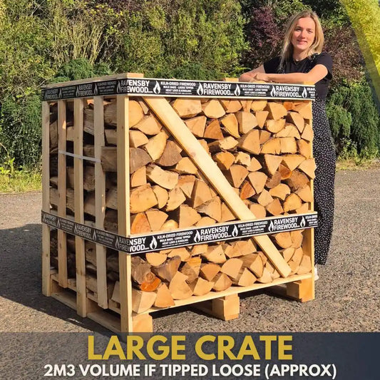 Person standing next to a large crate filled with kiln-dried firewood, with 'Ravensby Firewood' branding.
