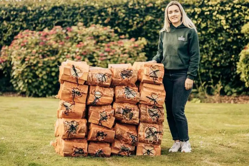 Emma from Ravensby Firewood standing next to a stack of hardwood log nets for use in wood burning stoves in Forfar